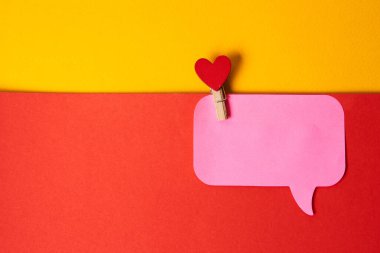 Bir mandalda kırmızı kalp ve pembe yapışkan bir not. Renkli bir arka plan.
