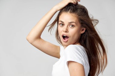 Ağzı açık bir kadın saçlarına ve beyaz tişörtüne dokunuyor. 