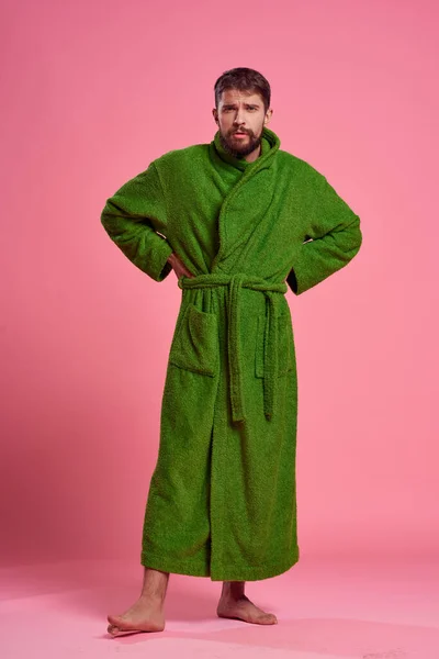 Emocjonalny mężczyzna w zielonym szlafroku w pełnym wzroście na różowym tle gestów z rękami do modelki — Zdjęcie stockowe