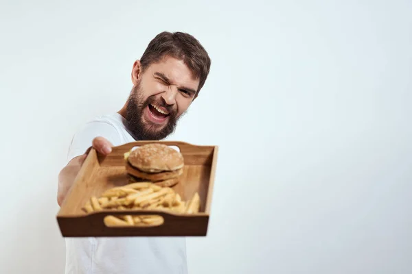 Homem com bandeja de madeira batatas fritas e hambúrguer fast food calorias modelo t-shirt branca — Fotografia de Stock