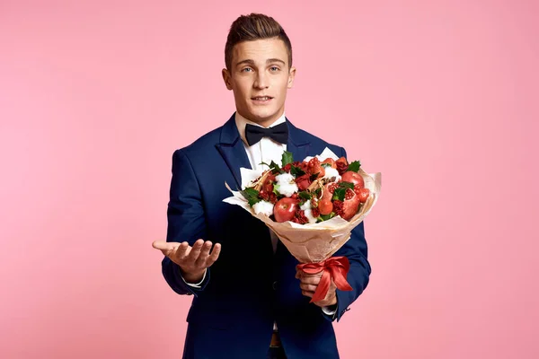 Bel homme dans un costume classique avec un bouquet de fleurs sur un fond rose vacances noeud papillon modèle — Photo