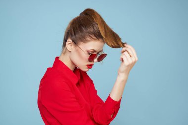 Mavi arka plandaki kırmızı gömlekli kadın yüz ve güneş gözlüklü kırmızı dudak makyajı modeli ile el ele tutuşuyor.