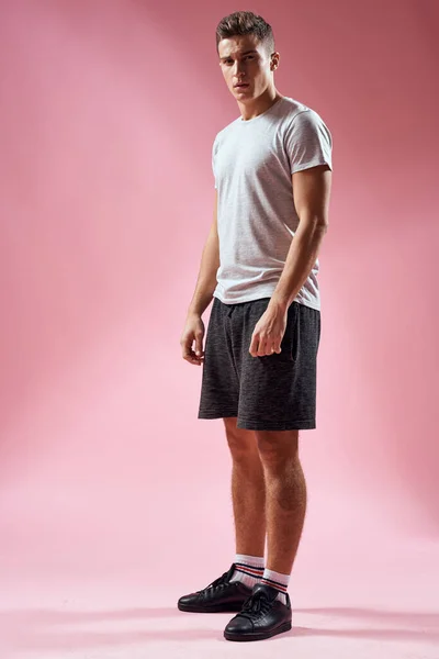 Een man in een sportbroek in een T-shirt en sneakers op een roze achtergrond in volle groei — Stockfoto