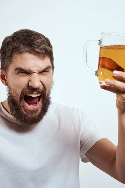 Ein bärtiger Mann mit einem Becher Bier auf hellem Hintergrund in einem weißen T-Shirt schnitt die Ansicht eines alkoholischen Getränks ab — Stockfoto