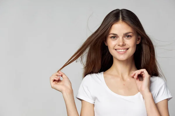 Glückliche brünette Frau berührt ihr Haar mit den Händen und lächelt auf hellem Hintergrund — Stockfoto