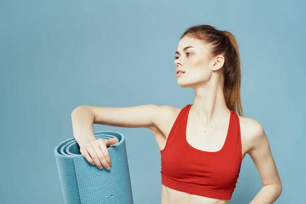 Sportieve vrouw trainingsmat in handen Rode tank top oefening blauwe achtergrond — Stockfoto