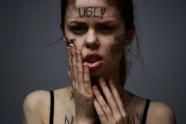 Förolämpad kvinna med arga inskriptioner på kroppen vidrör sig själv med händerna på en grå bakgrund aggression — Stockfoto
