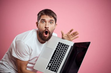 Açık dizüstü bilgisayarı olan beyaz tişörtlü bir adam elleri kırpılmış yeni teknoloji klavye monitörüyle jest yapıyor.