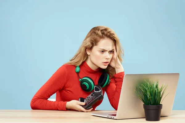 Mulher sentada em uma mesa na frente de um controlador de fones de ouvido laptop jogando estilo de vida on-line fundo azul — Fotografia de Stock