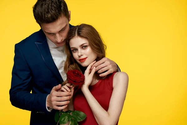 Milenci muž a žena s červenou růží v rukou objímání na žlutém pozadí romantika vztah láska rodina — Stock fotografie