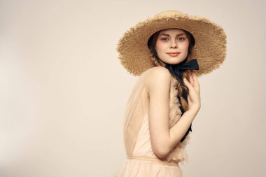 Hasır şapkalı, siyah kurdeleli ve arka planda açık bir elbise giyen hoş bir kız. Romantik bir model.