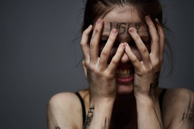 Gri arka planda kırıcı yazılar yazan üzgün kadın elleriyle kendine dokunuyor.