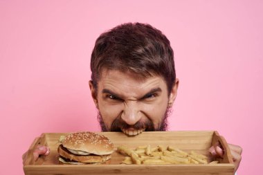 Elinde tepsi olan agresif bir adam. Hamburger kızartması. Pembe arka plan.