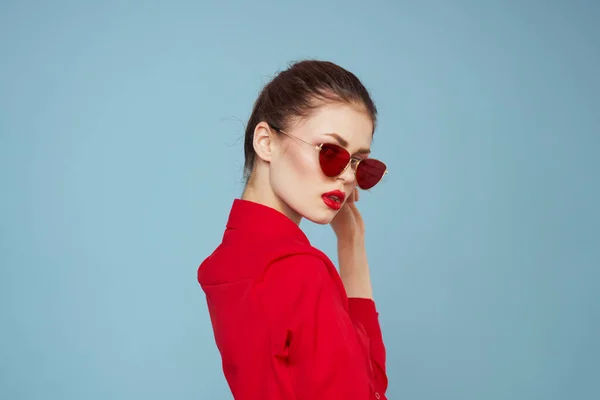 Woman in red shirt on blue background holds hands near face and sunglasses red lips makeup model — Stock Photo, Image