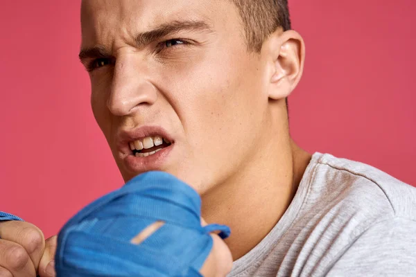 Hombre deportivo con guantes de boxeo azul y una camiseta sobre un fondo rosa practicando golpes recortados — Foto de Stock