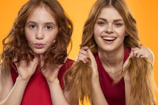Uma menina de cabelos vermelhos e uma mulher bonita em um fundo amarelo em vestidos vermelhos gesticular com as mãos e grimace — Fotografia de Stock