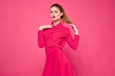 Pembe arka planda, parlak elbiseli, kızıl saçlı bir kadının portresi elleriyle el kol hareketi yapıyor.