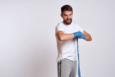 Beyaz tişörtlü sporcu. Kollarında mavi bandaj var. Egzersiz yapıyor.