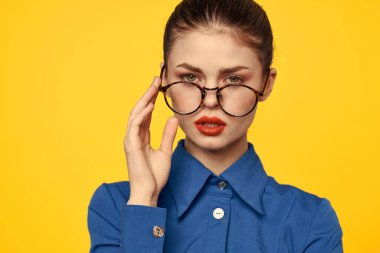 Mavi gömlekli, gözlüklü, yüzünde parlak makyajlı bir kadın elleriyle işaret ediyor.