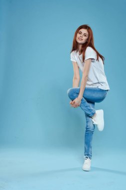 Beyaz tişörtlü, mavi kot pantolonlu, tam gelişmiş stüdyo mavi arka planlı güzel bir kadın.