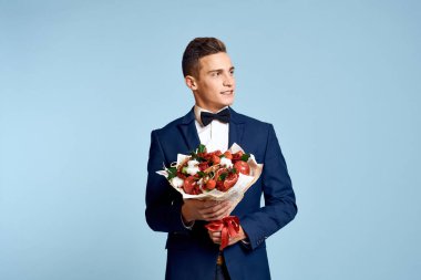 Bir buket çiçekli ve mavi arka planda papyonlu romantik bir adam.