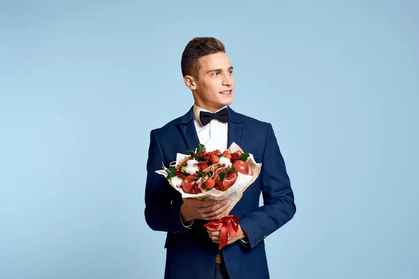 Romantisk man med en bukett blommor och i en fluga på en blå bakgrund beskärd utsikt — Stockfoto