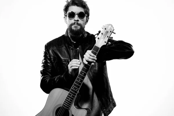 A man holds a guitar in his hands black leather jacket dark glasses music performance light background — Stock Photo, Image