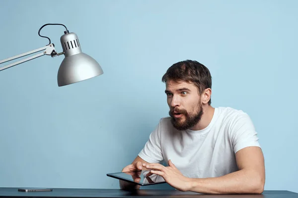 Homem com tablet à mesa dentro de casa e lâmpada escritório freelancer fundo azul — Fotografia de Stock