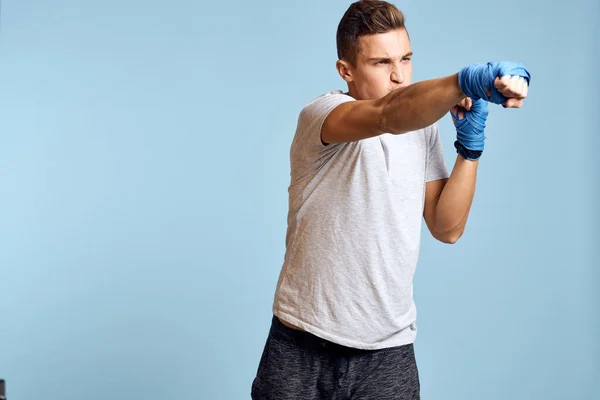 Uomo sportivo in guanti da boxe blu e t-shirt su sfondo blu praticando pugni vista ritagliata — Foto Stock