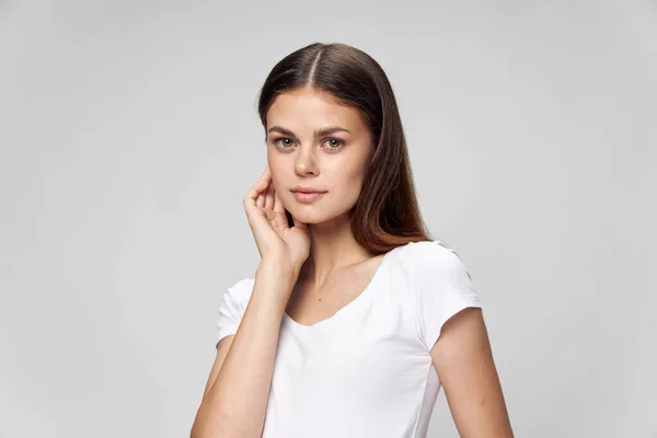 Una bruna con i capelli lunghi tiene una mano vicino al viso, una t-shirt bianca — Foto Stock