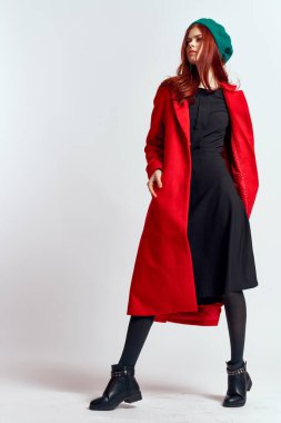 Kırmızı ceketli, şapkalı, açık renk arka planda siyah çizmeli, duygusal bir kadın model.