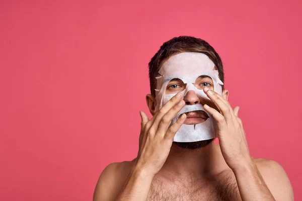 Man met blote schouders in een wit masker heldere huid roze achtergrond — Stockfoto