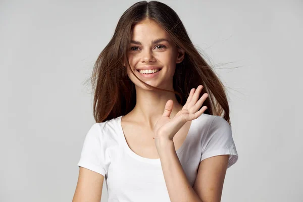 Outstanding woman in a white T-shirt gestures with her hand on a light background close-up — Stock Photo, Image