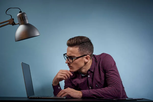 Um homem em uma camisa com um laptop na mesa é um gerente no escritório e um modelo de armário de lâmpadas — Fotografia de Stock