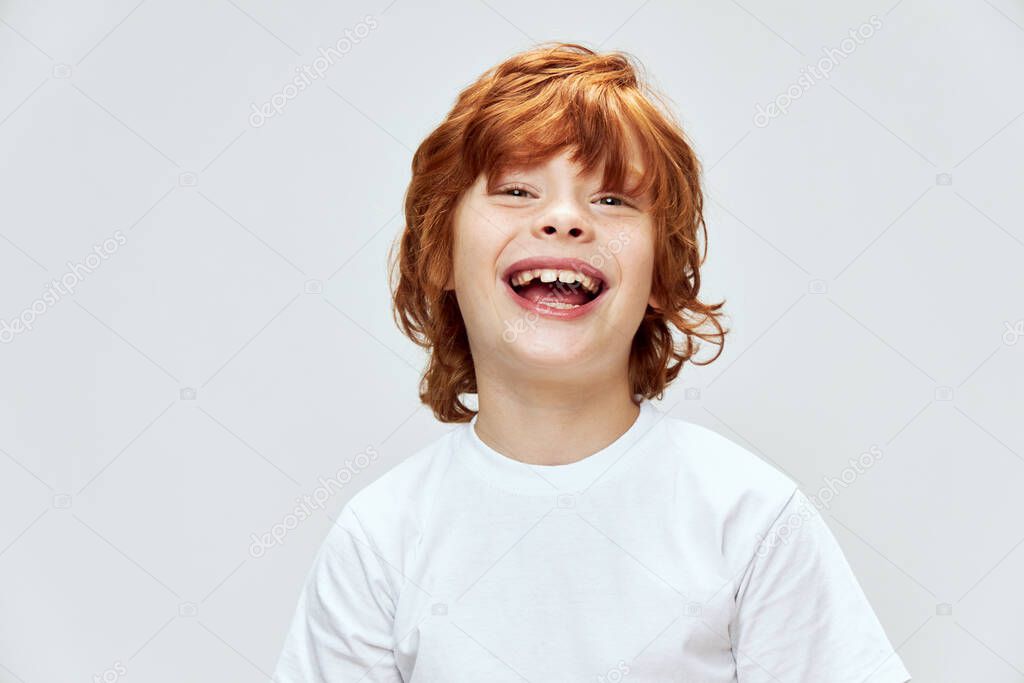 red-haired child with wide open smile in white t-shirt gray background 
