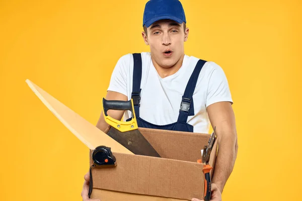 Pracovník s krabicí v ruce nářadí nakladač žluté pozadí — Stock fotografie
