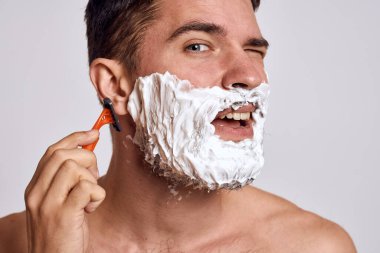 Yüzünde beyaz tıraş köpüğü olan yakışıklı bir adam ve jilet gibi omuzları olan temiz bir cilt.