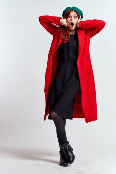 emotional woman in a red coat and with a hat in full growth on a light background black boots pose model