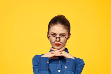 Mavi gömlekli, gözlüklü, yüzünde parlak makyajlı bir kadın elleriyle işaret ediyor.