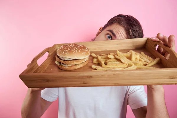 Mann mit einem Tablett mit Lebensmitteln in der Hand Hamburger-Pommes und Fast-Food-Kalorien rosa Hintergrund Porträt Nahaufnahme — Stockfoto