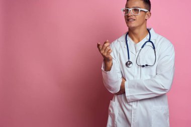 Pembe bir arka planda steteskop ve yüzünde gözlük olan tıbbi önlüklü bir erkek doktor.