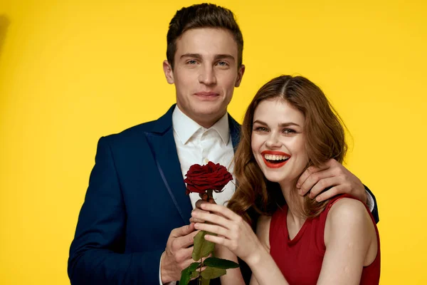 Älskare man och kvinna med en röd ros i händerna kramas på en gul bakgrund romantik relation kärlek familj — Stockfoto