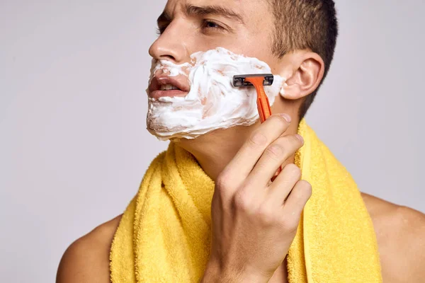 Een man met een gele handdoek op zijn schouders en een oranje scheermes wit schuim schone huid — Stockfoto