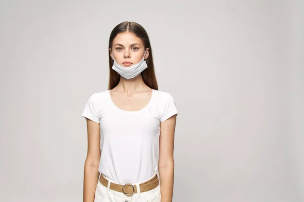 귀에는 의료용 마스크를 쓰고 흰색 티셔츠를 입은 여성이 베이지 벨트 앞을 보고 있습니다 — 스톡 사진