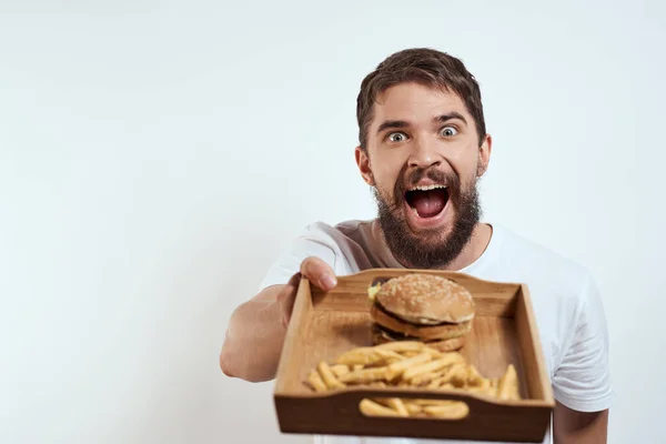 Homem com bandeja de madeira batatas fritas e hambúrguer fast food calorias modelo t-shirt branca — Fotografia de Stock