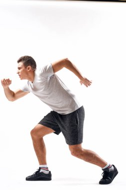 Hafif bir geçmişi olan atletik bir adam tam boy ve koşu şortu spor ayakkabısı tişörtü giyiyor.