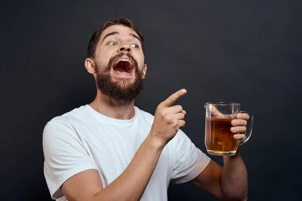Homem com uma caneca de cerveja em suas mãos emoções divertido estilo de vida branco t-shirt escuro isolado fundo — Fotografia de Stock