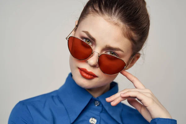 Donna alla moda in occhiali da sole e una camicia blu gesticolando con le mani su uno sfondo chiaro vista ritagliata — Foto Stock