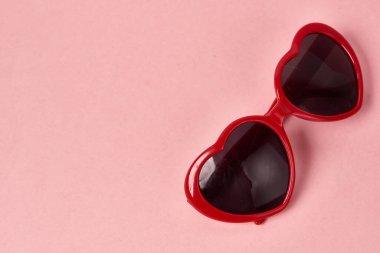 Kalp şeklinde güneş gözlüğü, pembe arkaplanda kırmızı çerçeveler.