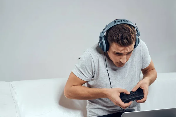 Un hombre en el sofá delante de un portátil con un joystick en un auricular de tecnología de videojuegos —  Fotos de Stock